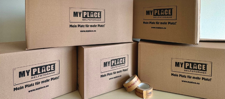 5 verschieden große Kartons sind gestapelt, auf ihnen ist groß das Logo von MyPlace-SelfStorage zu sehen, davor liegen zwei Rollen Klebeband