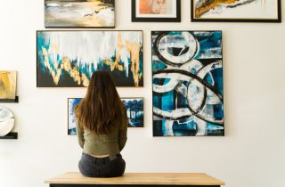 Eine Frau sitzt auf einer Bank vor vielen bunten Bildern an der Wand.